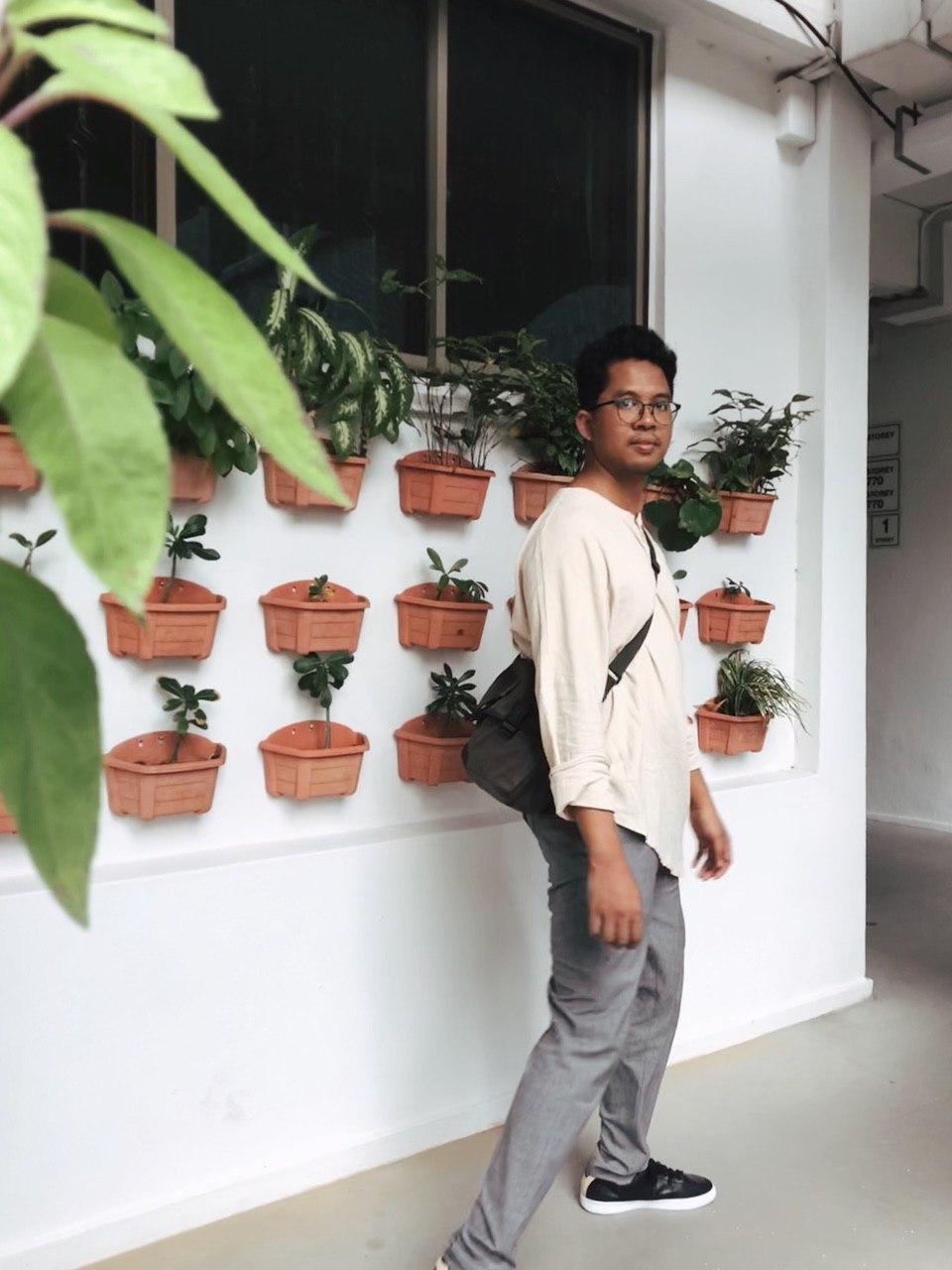 Photo of him walking in a corridor with hanging plants.